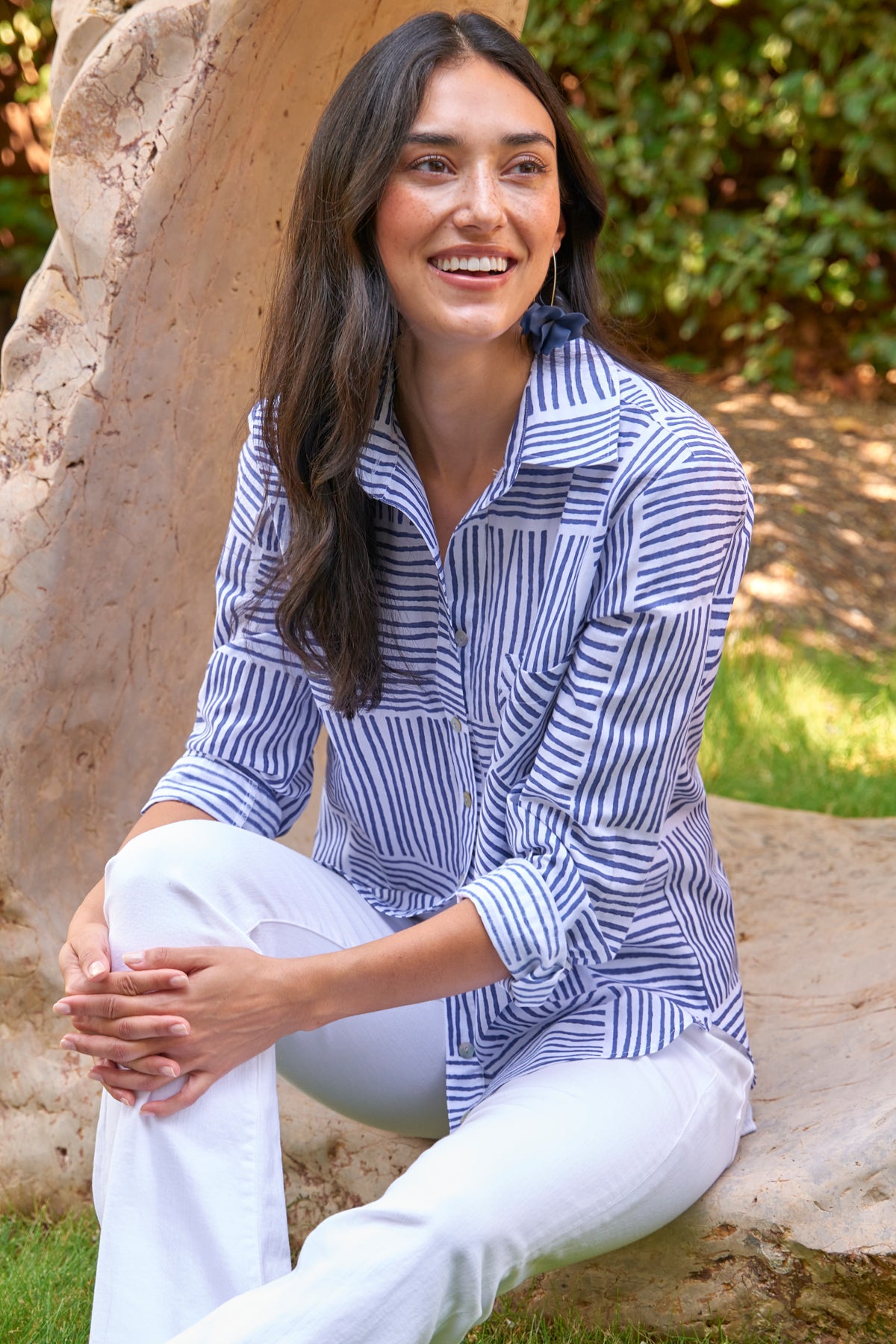 Woman wearing a blue and white striped shirt and white pants sitting outdoors.