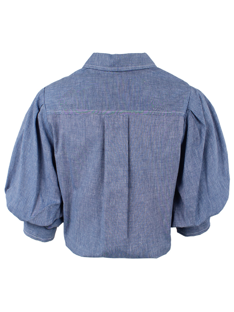 A rear view of the Finley Bomba blouse, a pale blue denim button down women's blouse with a front-hem twist and short blouson sleeves.