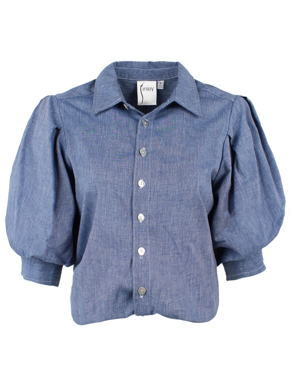 A front view of the Finley Bomba blouse, a pale blue denim button down women's blouse with a front-hem twist and short blouson sleeves.