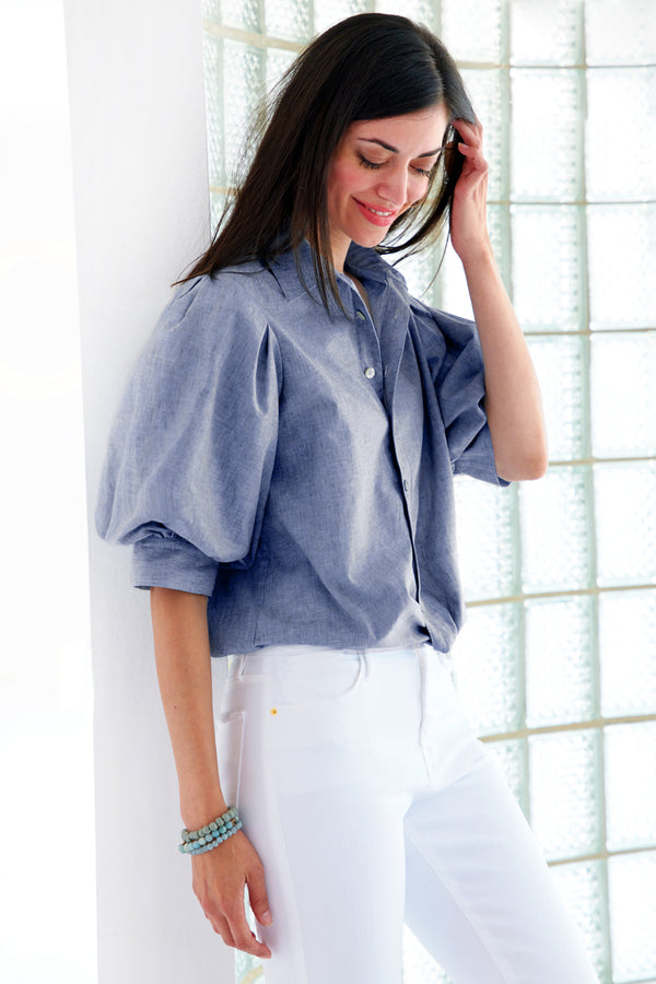 A model wearing the Finley Bomba blouse, a pale blue denim button down women's blouse with a front-hem twist and short blouson sleeves.