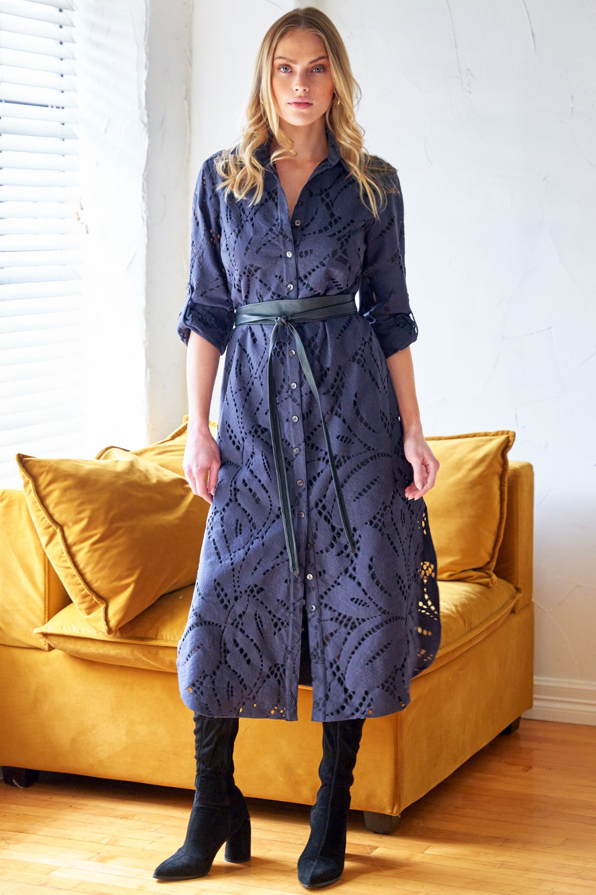 Woman wearing a blue lace dress standing in a room with a yellow couch.
