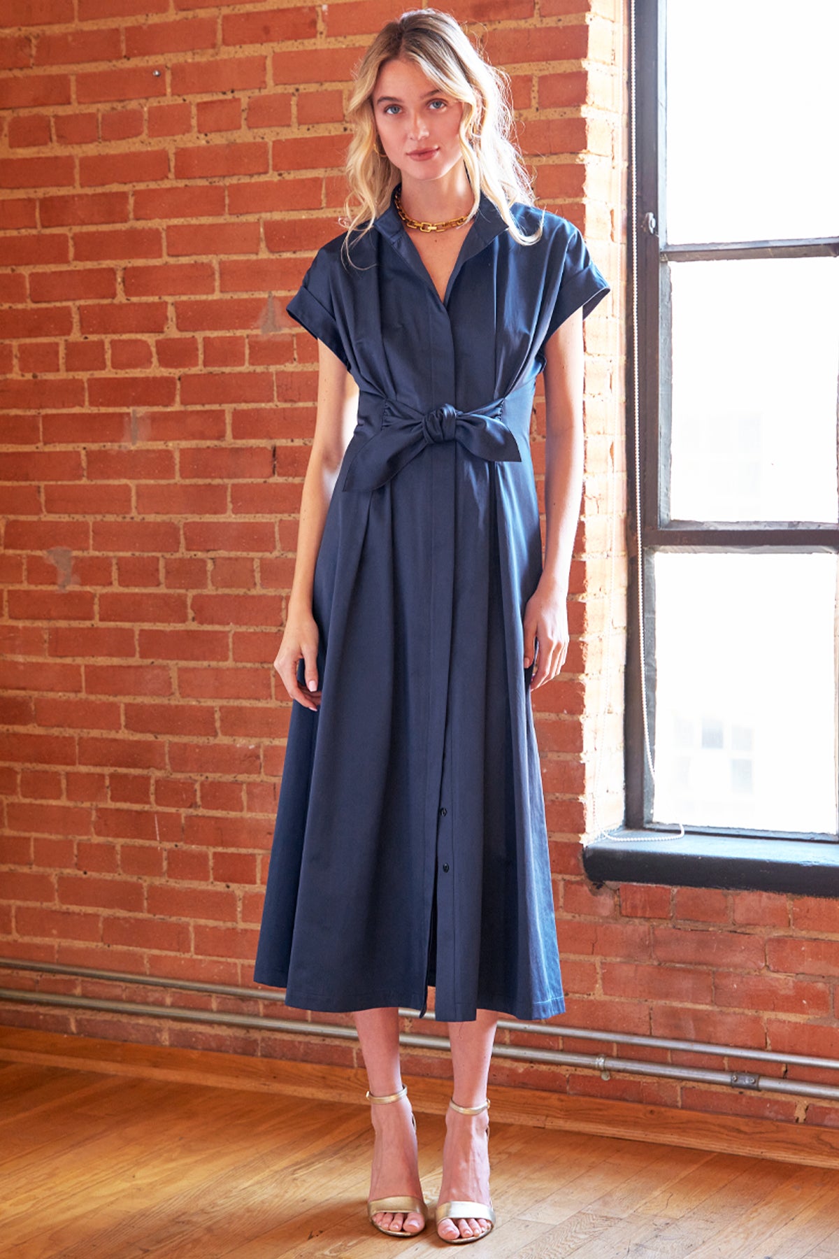 Woman wearing a navy dress standing in front of a brick wall.