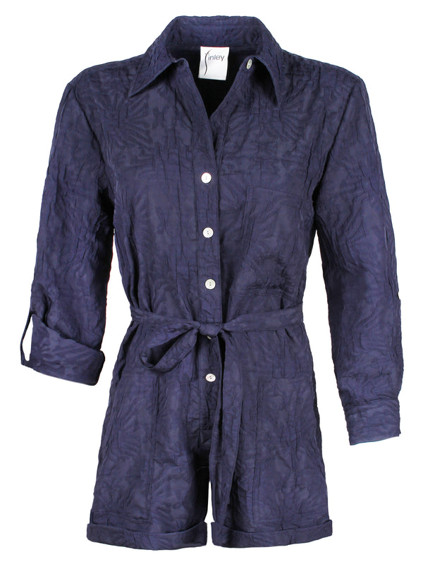 A front view of the Finley Romper, a navy jacquard one-piece button down romper with a tie front and barrel cuffs.