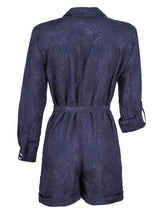 A rear view of the Finley Romper, a navy jacquard one-piece button down romper with a tie front and barrel cuffs.