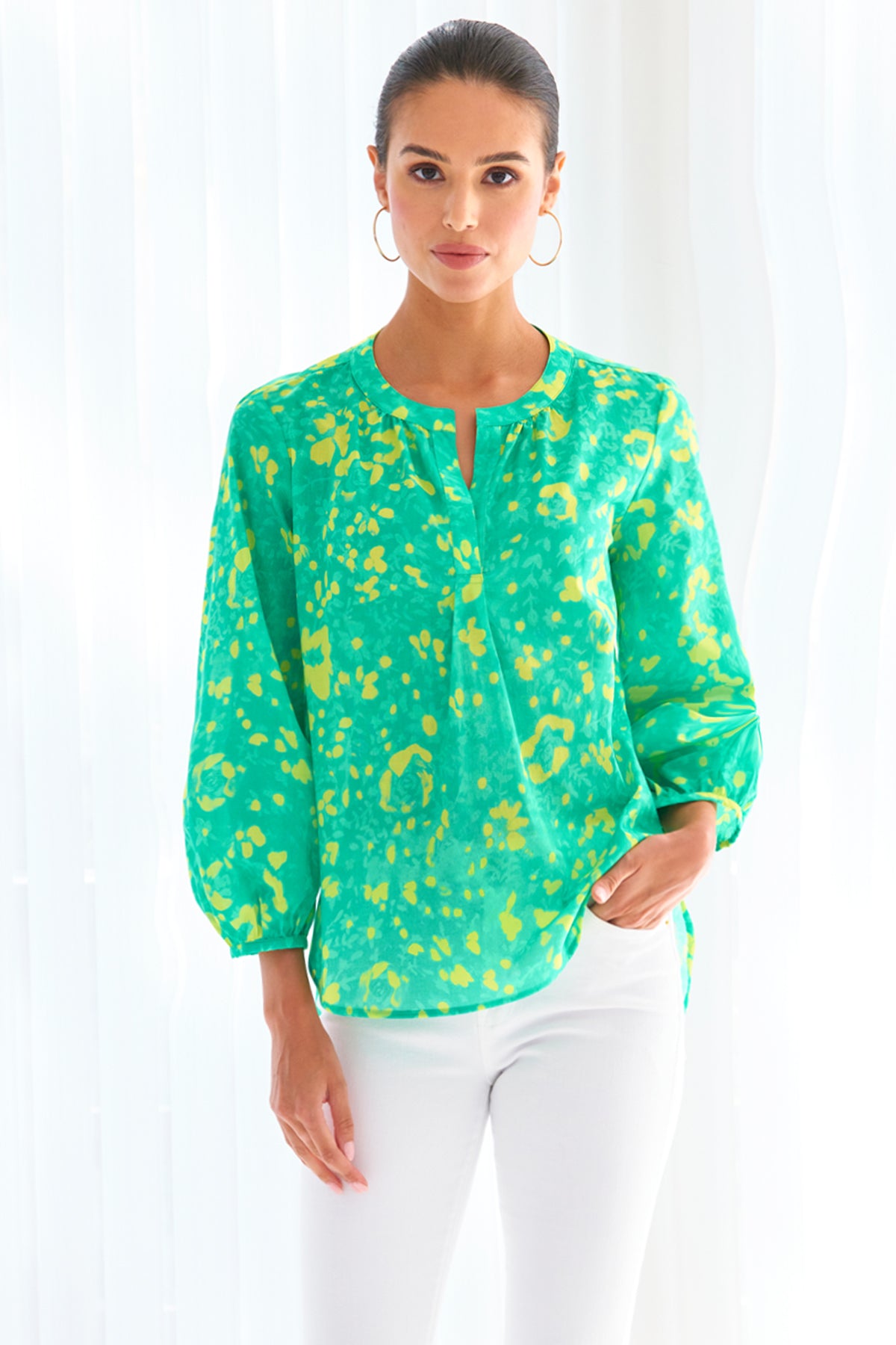 A model wearing the Finley Stephanie top, a v-neck blouse with bracelet sleeves and a bright green and yellow floral print.