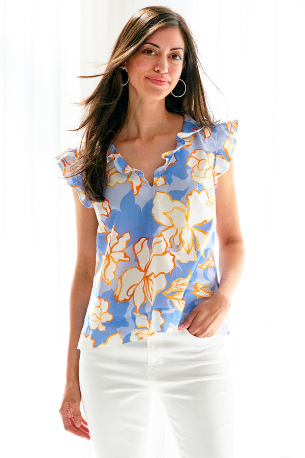 A model wearing the Ava blouse, a cotton popover women's blouse with ruffle sleeves, a v-neckline, and an abstract blue floral print.