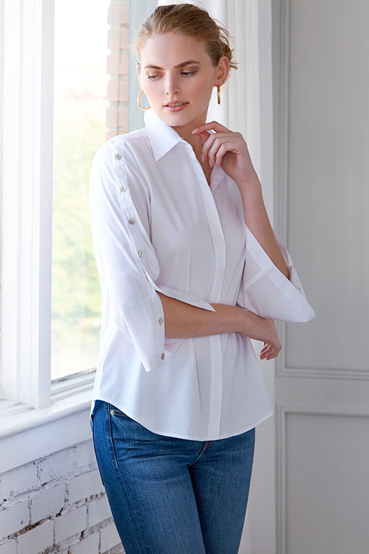 Woman wearing a white blouse with rolled-up sleeves and blue jeans indoors.