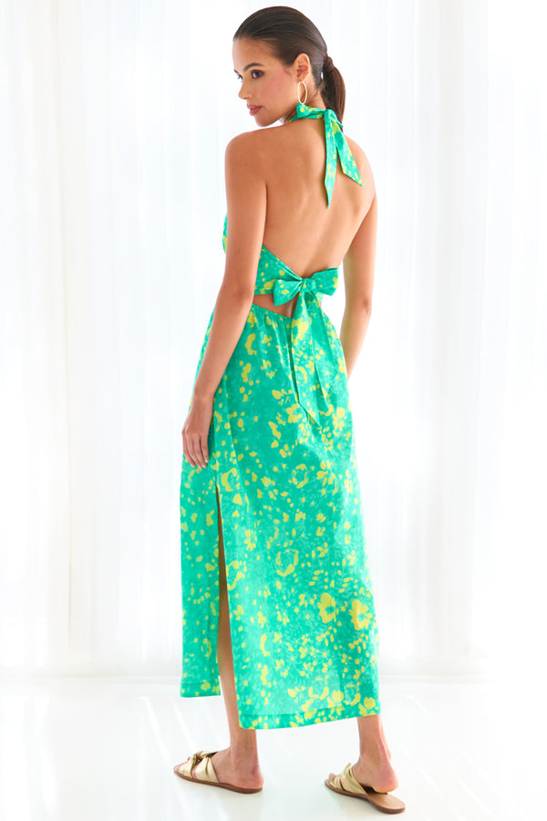 A model wearing the Finley Cameron, a cotton halter top tie front maxi dress with a bright green floral motif.