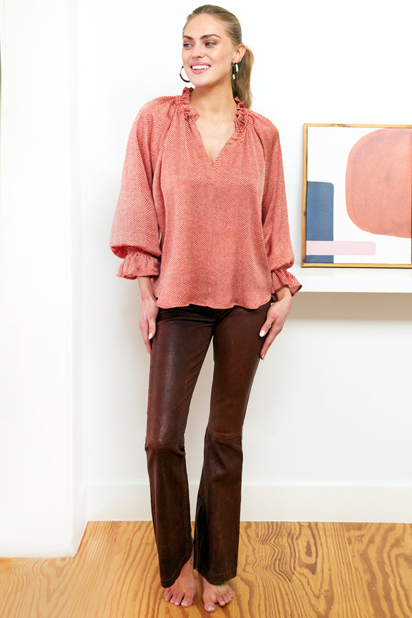 A model wearing the Finley Candace, an oversize fit brick red v-neck popover blouse with puff sleeves and a ruffle collar.