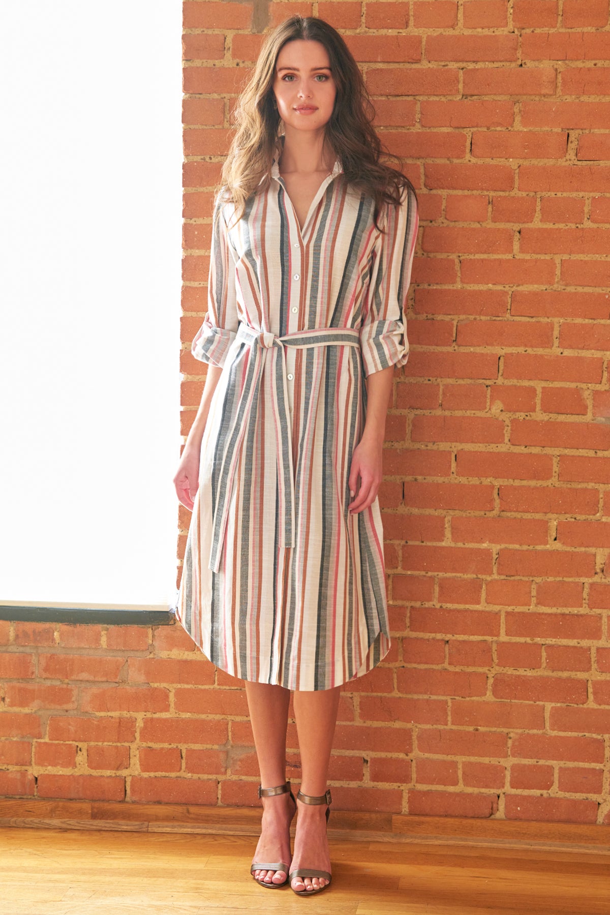 Woman wearing a striped dress standing against a brick wall.