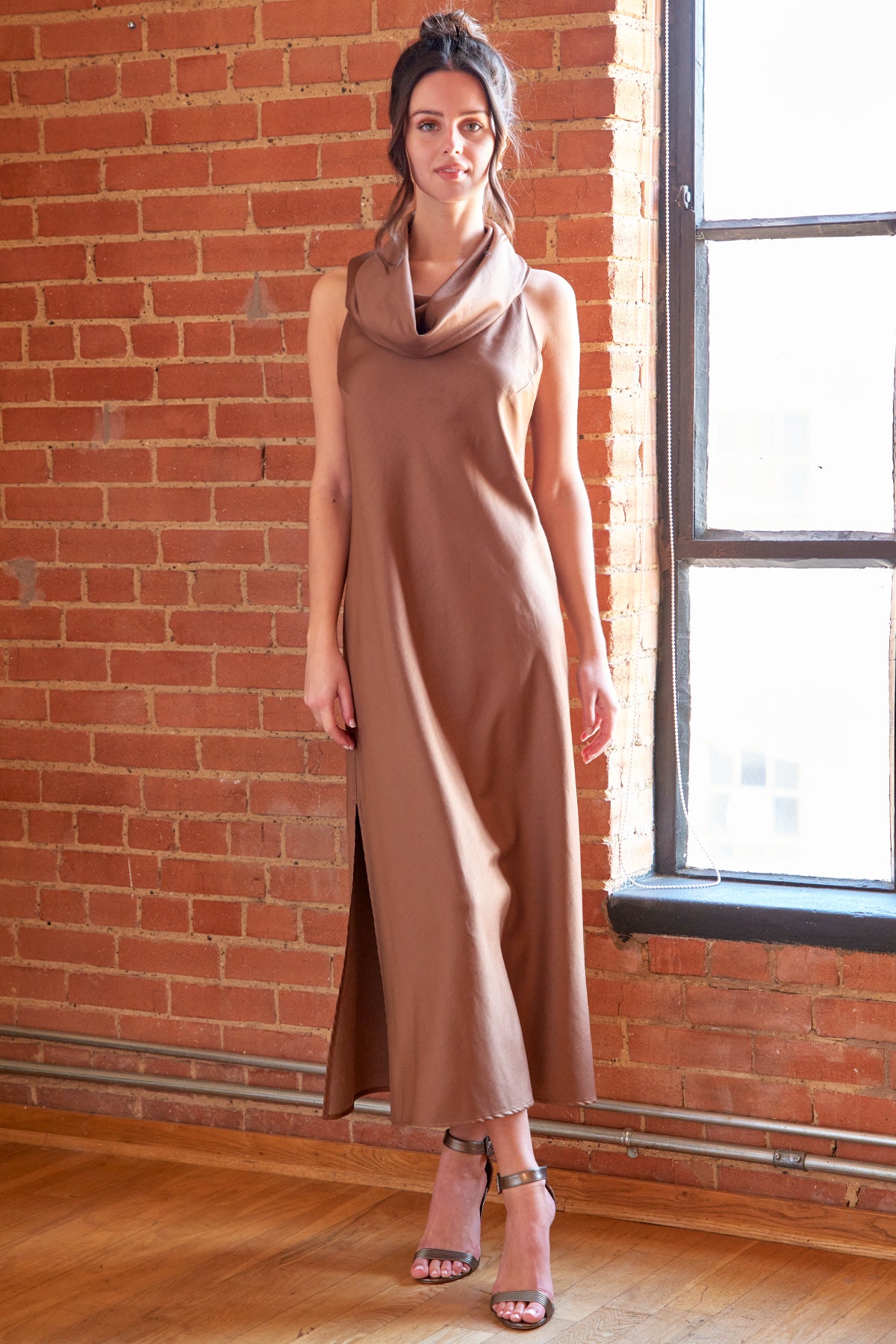 Woman wearing a brown sleeveless dress standing in front of a brick wall.