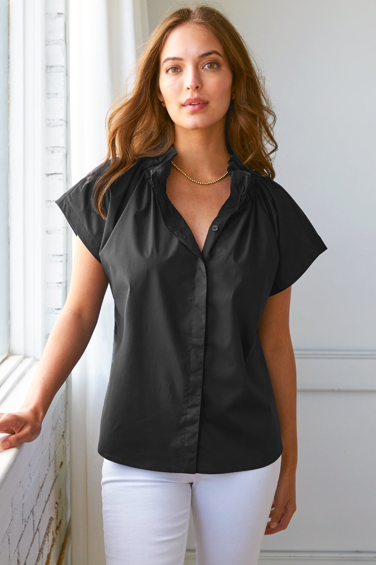 Model wears Finley Jenny black silky poplin top with ruched ruffle detail and stand collar.

