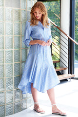 A young woman wearing the Finley Leonardo dress, a sky blue tie front button down long sleeves with a bias flounce design.