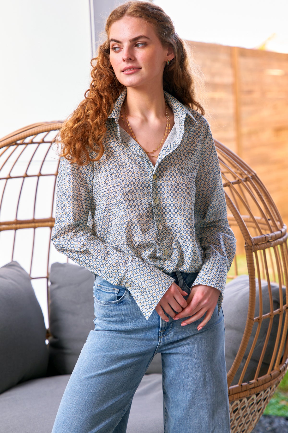 A model wearing the Finley Moxie blouse, a womens cotton sateen blouse with a front-twist hem, a relaxed fit, and a geometric blue print.