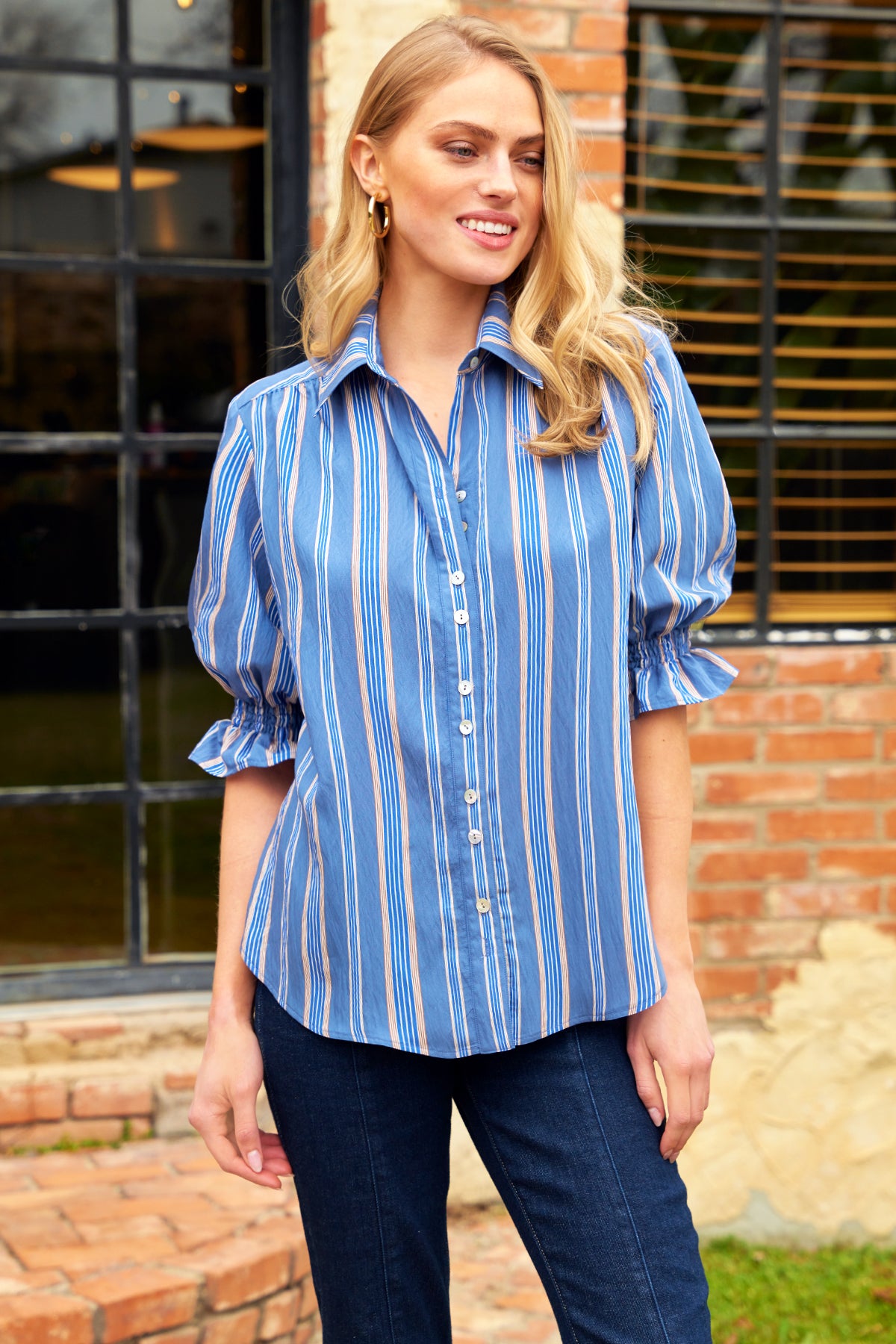 Woman wearing a blue striped shirt and jeans standing outdoors.