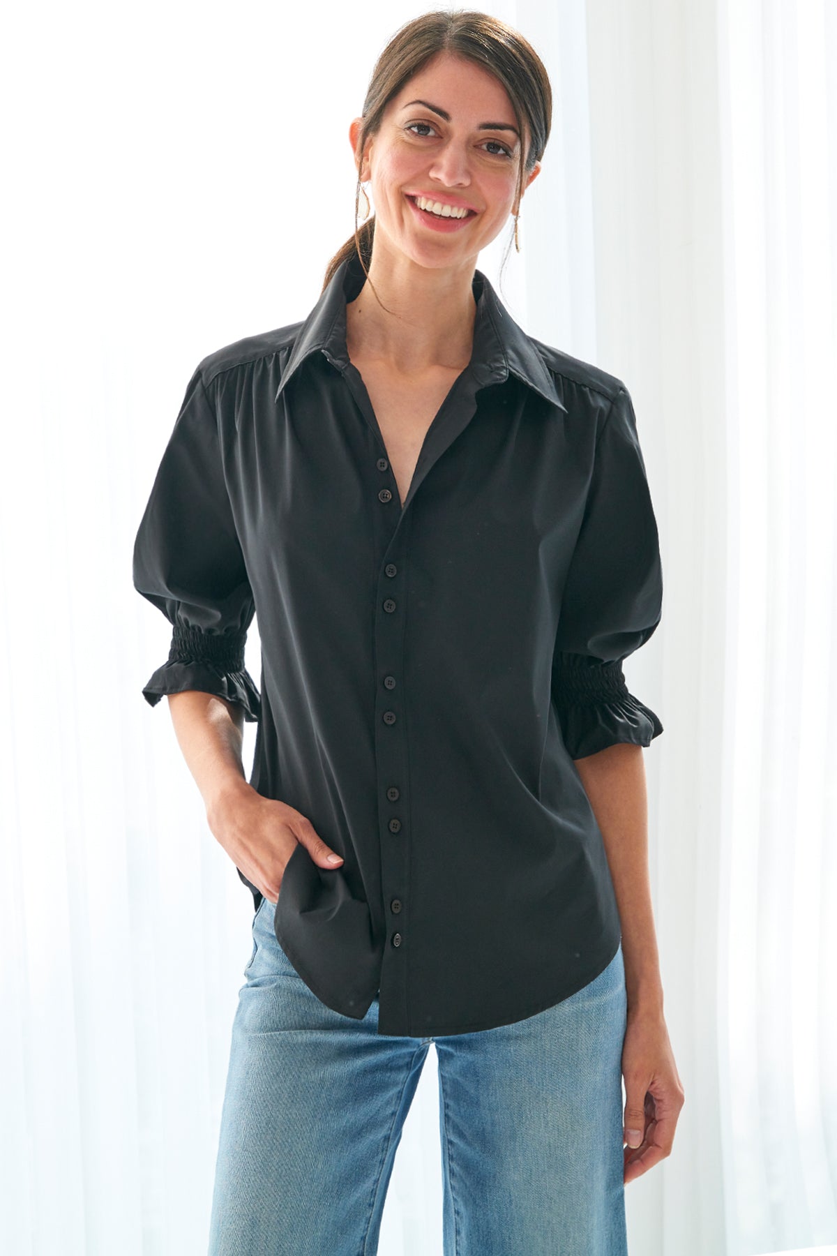 A model wearing the Sirena shirt in classic black, styled with shirred shoulders and puffed sleeves.
