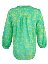 A rear view of the Finley Stephanie top, a v-neck blouse with bracelet sleeves and a bright green and yellow floral print.