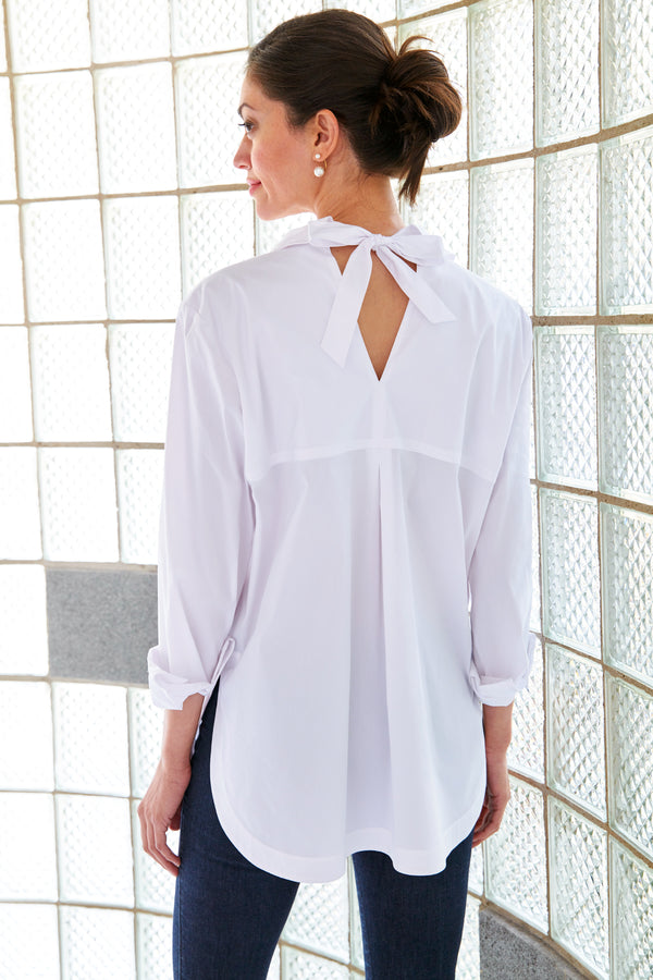 A model wearing the Finley Sylvie blouse, a white poplin blouse with a self-tie cutout back and a relaxed shape.