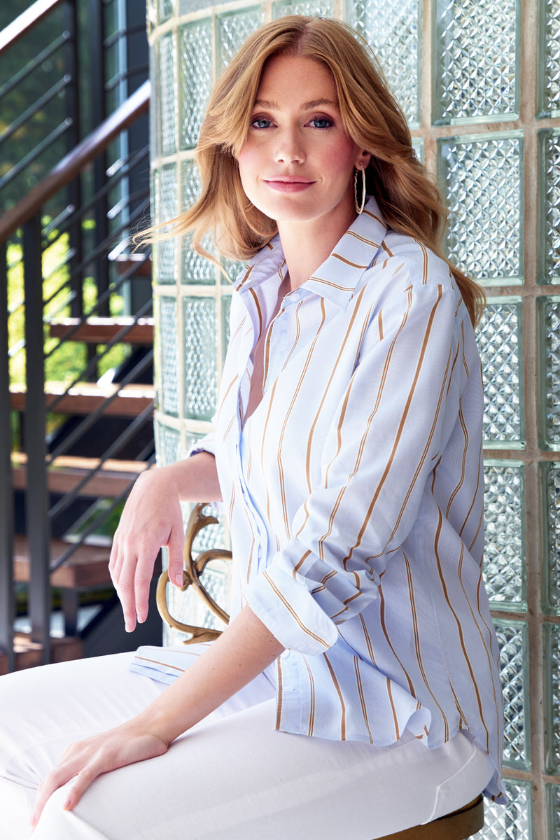 A model wearing the Finley Alexa blouse, a oversize button-down womens shirt with blue and tan stripes.