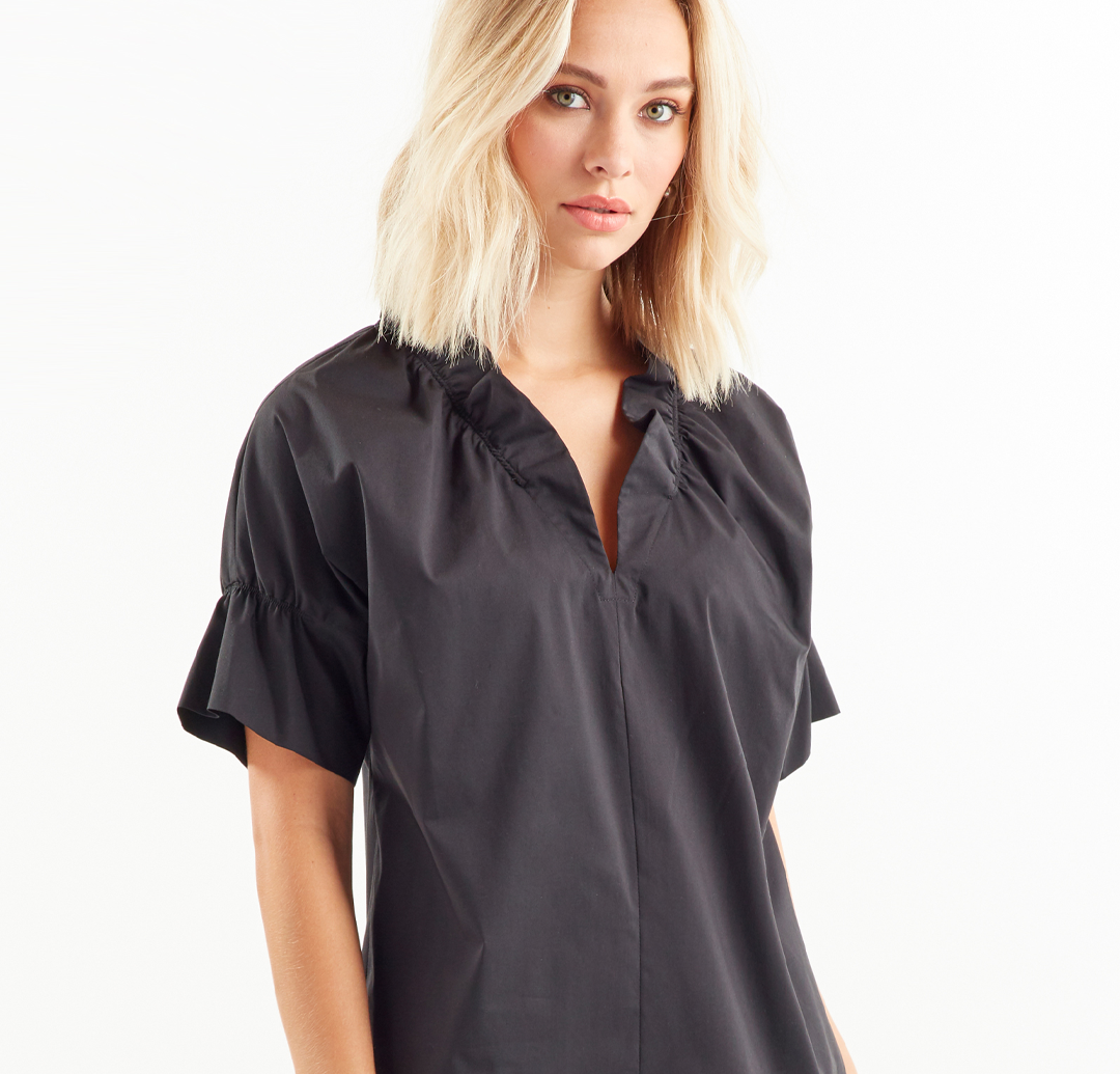A fashion model wearing the Finley Crosby blouse, a black cotton short sleeve popover v-neck blouse with a crisp, tailored fit.