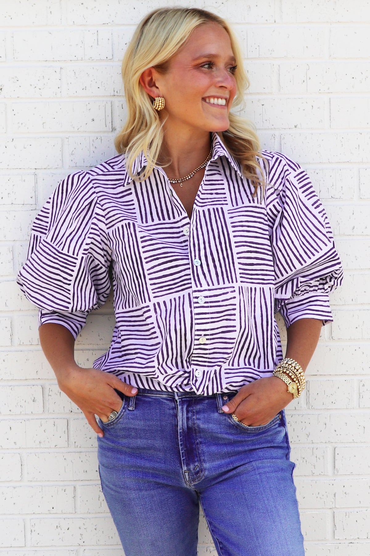 Woman wearing a striped shirt and blue jeans against a white brick wall