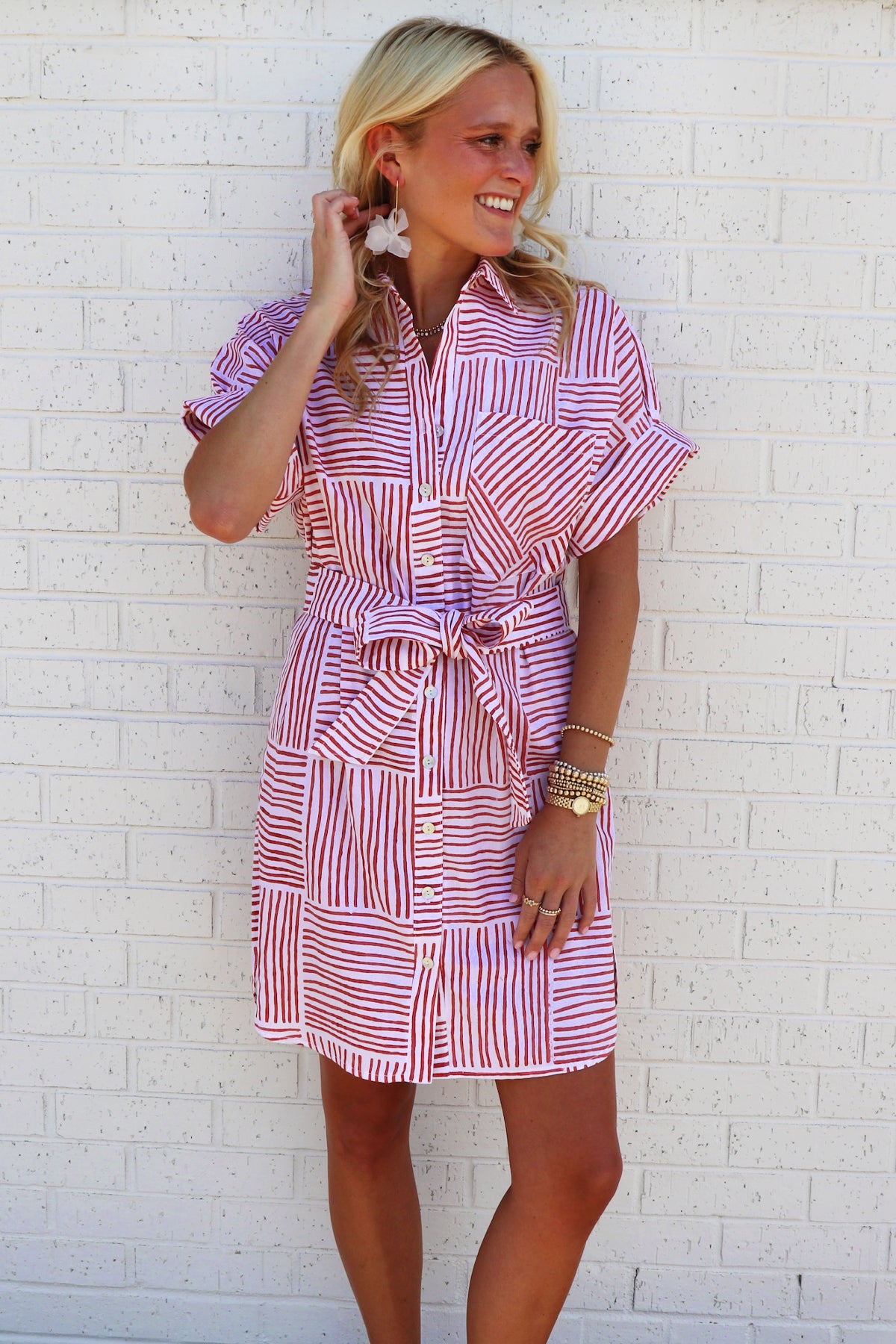 Woman wearing a red and white striped dress against a white brick wall.