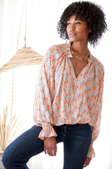 The Finley Brette blouse, an oversize popover puff sleeve v-blouse with ruffle trim and an orange and white leaf pattern.