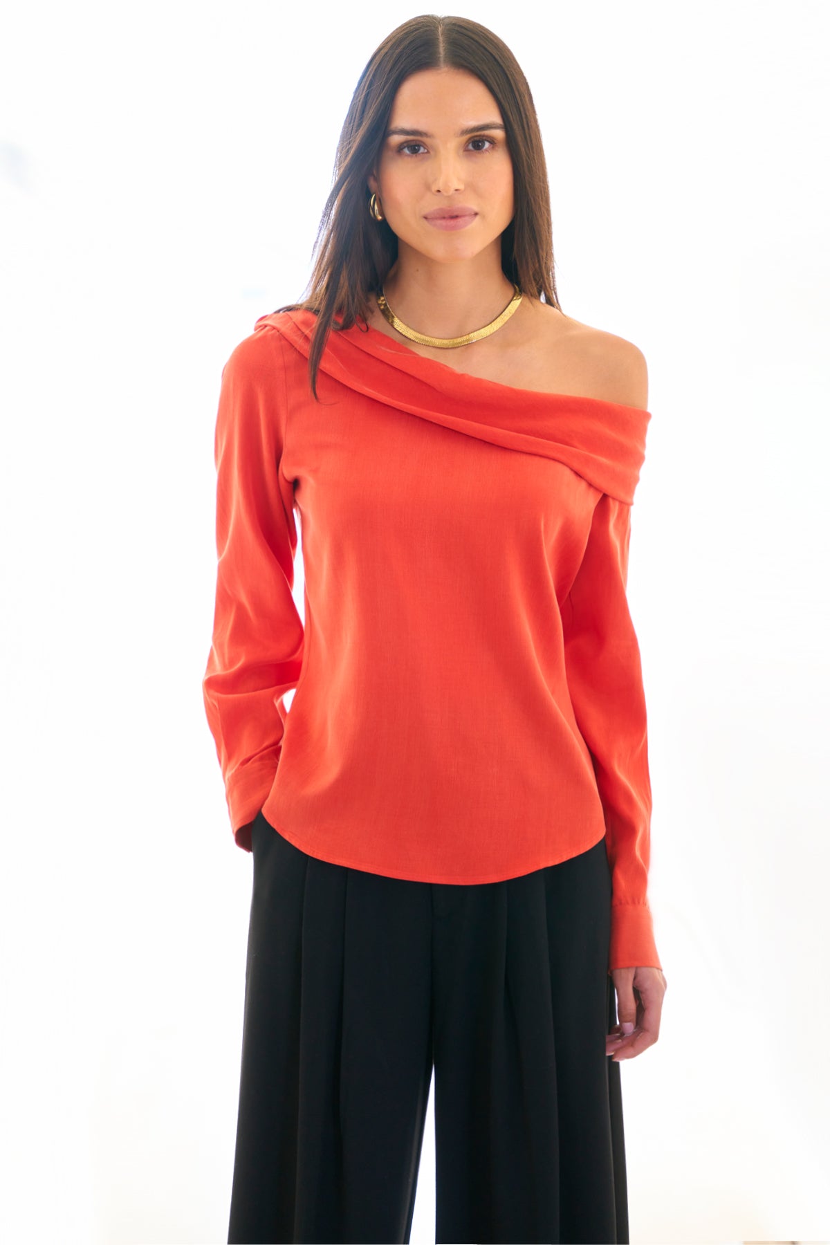 A model wearing the Dani shirt, featuring long sleeves, an off-shoulder foldover neckline, cupro cotton fabric in flame red, and a relaxed shape.
