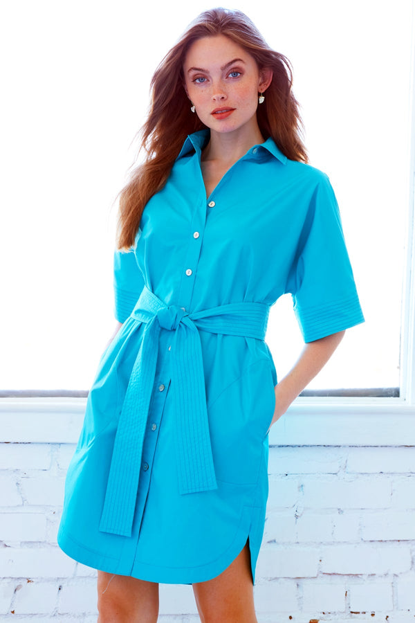 A model wearing the Finley Dolman dress, a turquoise short-sleeved button-down shirt dress with a detachable belt.
