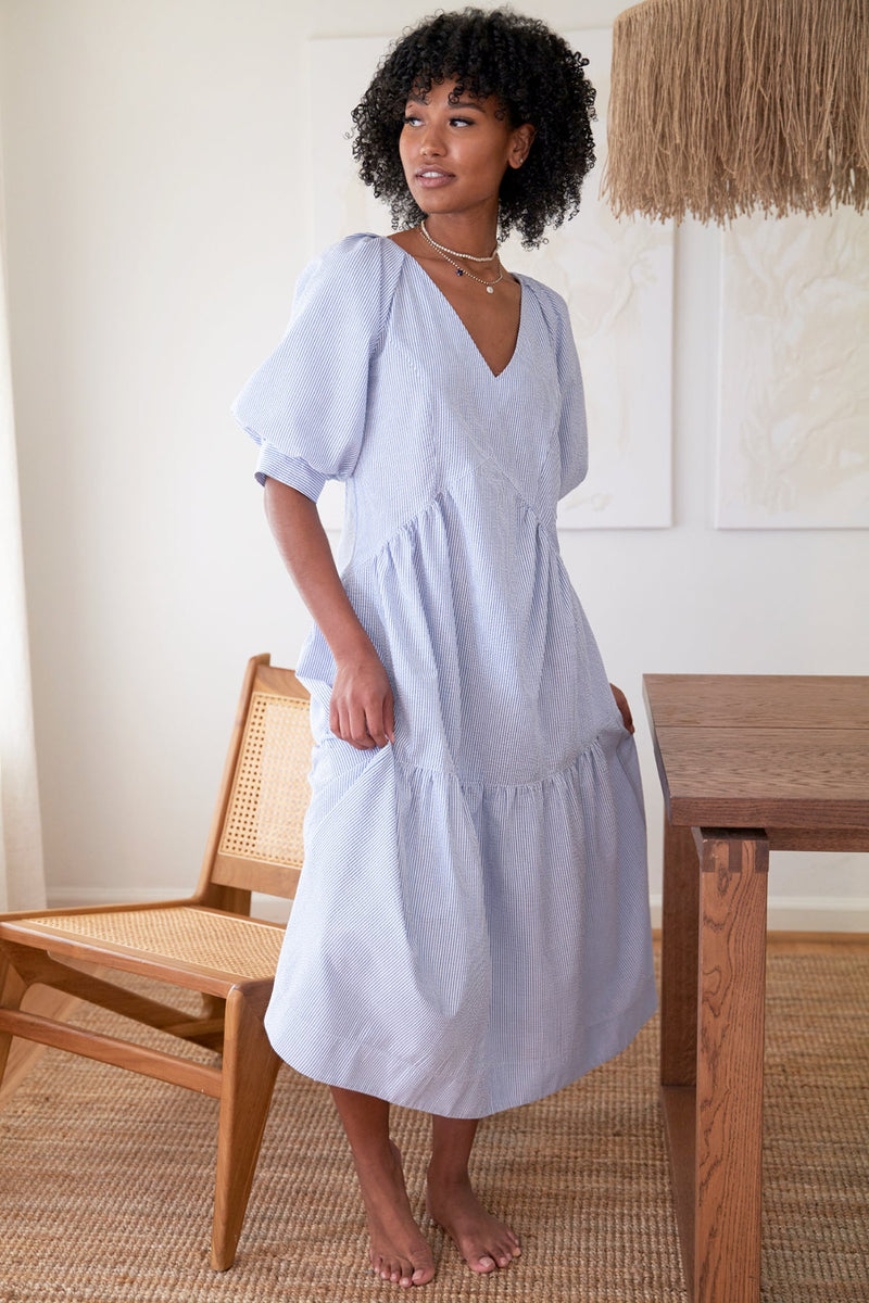 A Black supermodel wearing Finley Paloma dress, a green seersucker stripe v-neck maxi dress with puff short sleeves and ruffle hem.