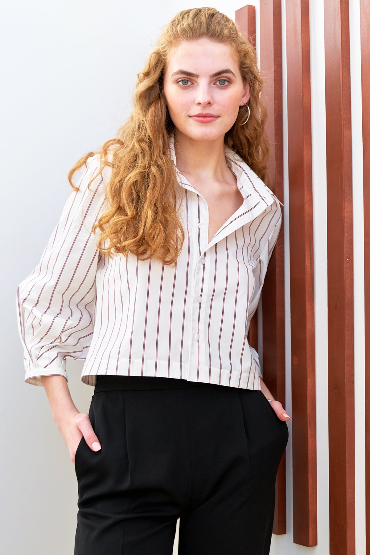 A model wearing the Finley Emmy, a cropped poplin shirt with a relaxed shape, pleated cuffs, and olive green pinstripes.