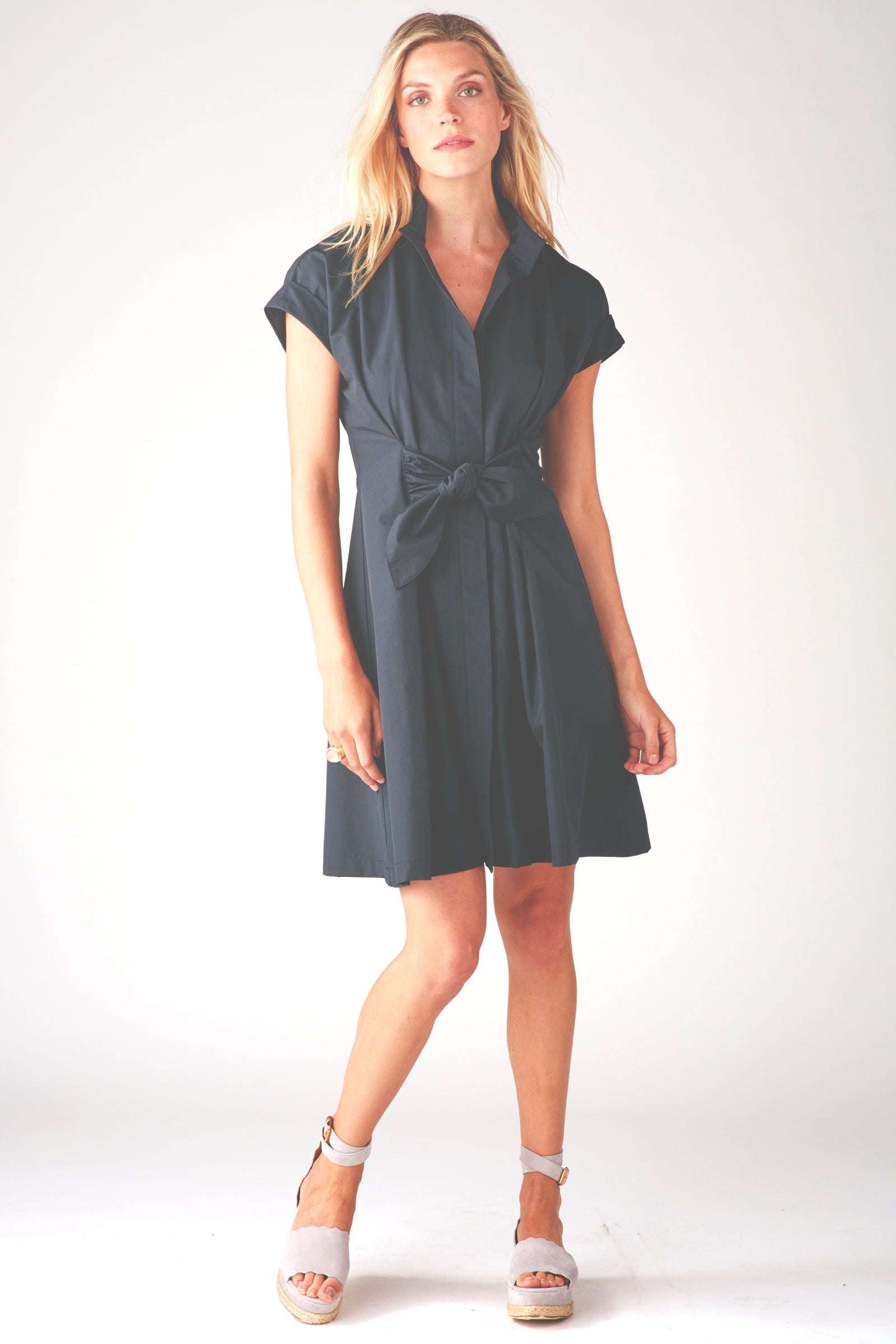 Model wears Finley Rocky black fit-and-flare shirt dress with tie front and cap sleeves. Below-knee length.

