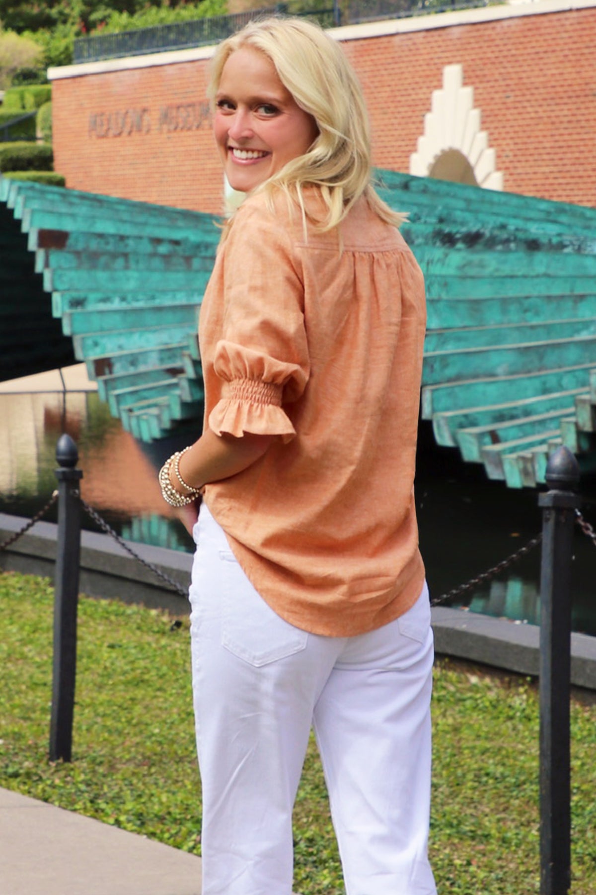 A model wearing the Sirena shirt in rust orange, featuring elbow-length puff sleeves, a hemp cotton blend, spread collar, and a relaxed shape.
