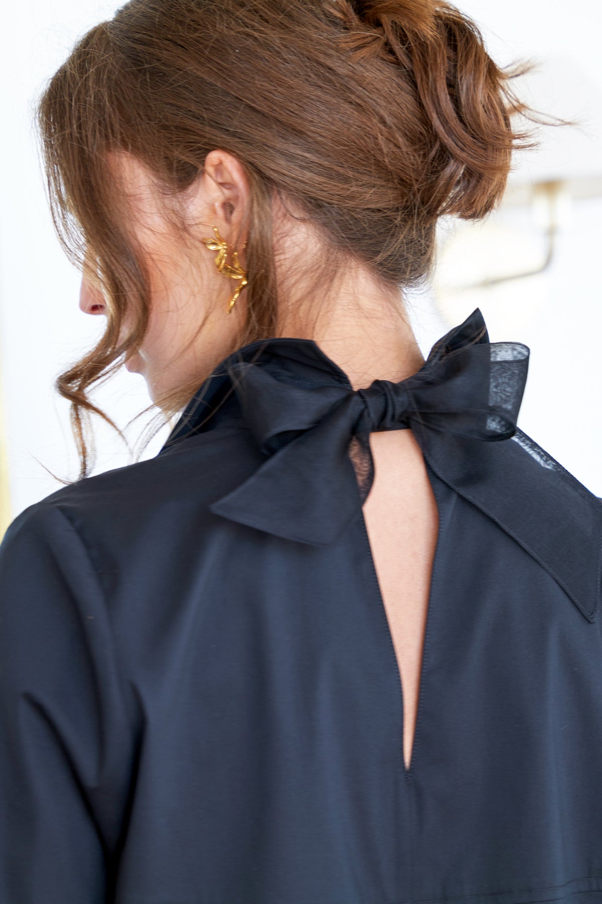 A different model perspective of the Sylvie shirt with a cutout back self-tie, black organza bow, relaxed contour, and long sleeves.
