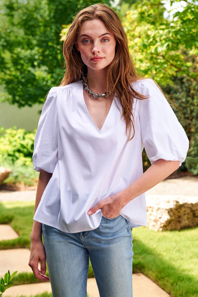 A model wearing the Tish blouse, a white silky poplin pullover casual blouse with puffy sleeves and a relaxed fit.