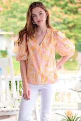 The Finley Tish top, a 100% cotton v-neck popover blouse with short puff sleeves and an orange floral pattern.