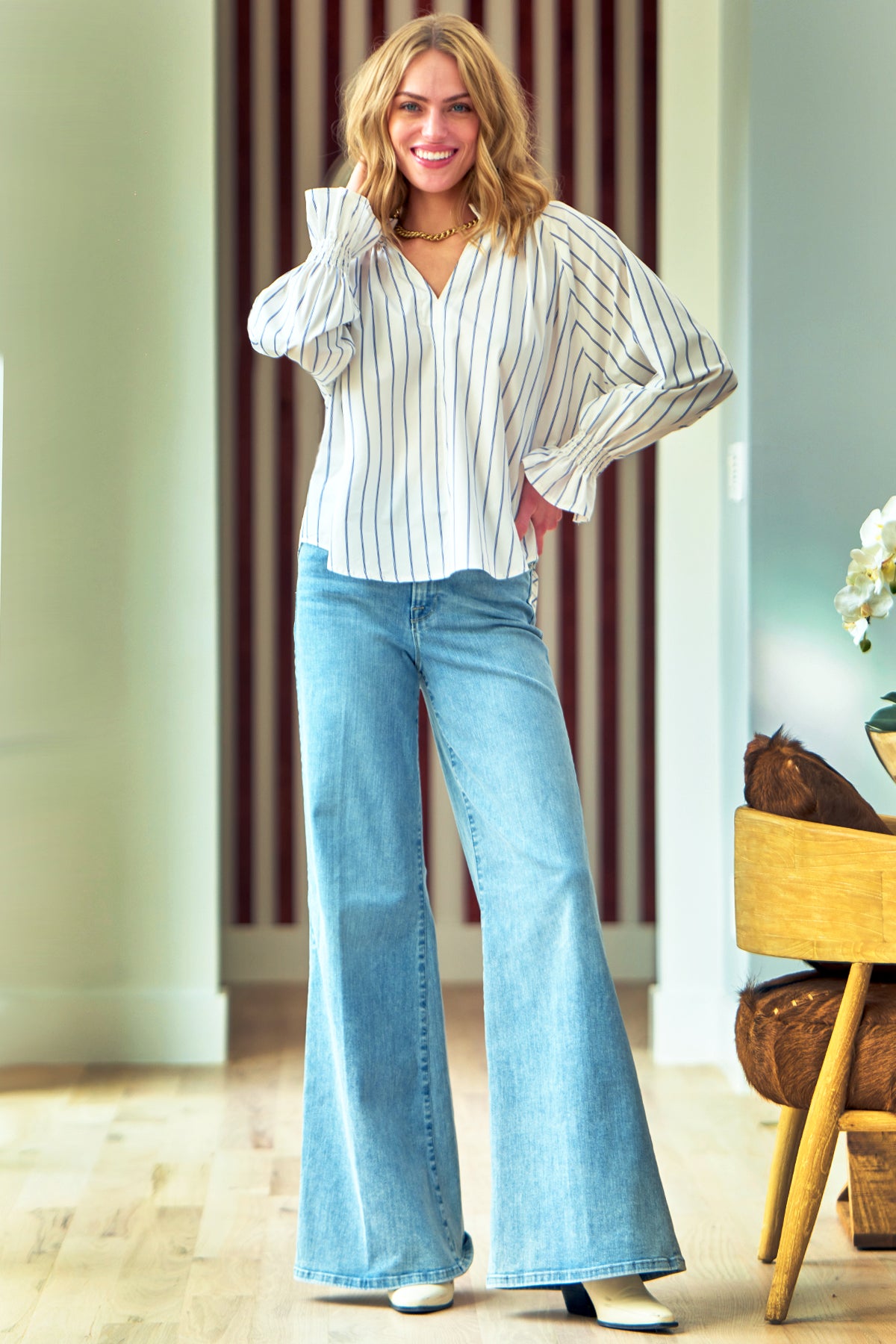 A model wearing the Finley Candace blouse, a v-neck ruffle popover poplin top with blue pinstripes.