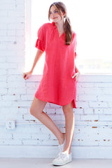 A model wearing the Finley Crosby shirt dress, a washed linen dress with ruffled sleeves and collar and a coral pink color.
