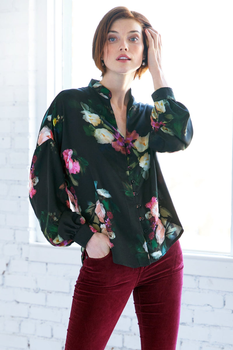 A model wearing the Finley band collar blouse, a button down long sleeve shirt with a drop shoulder and a Dutch floral print.