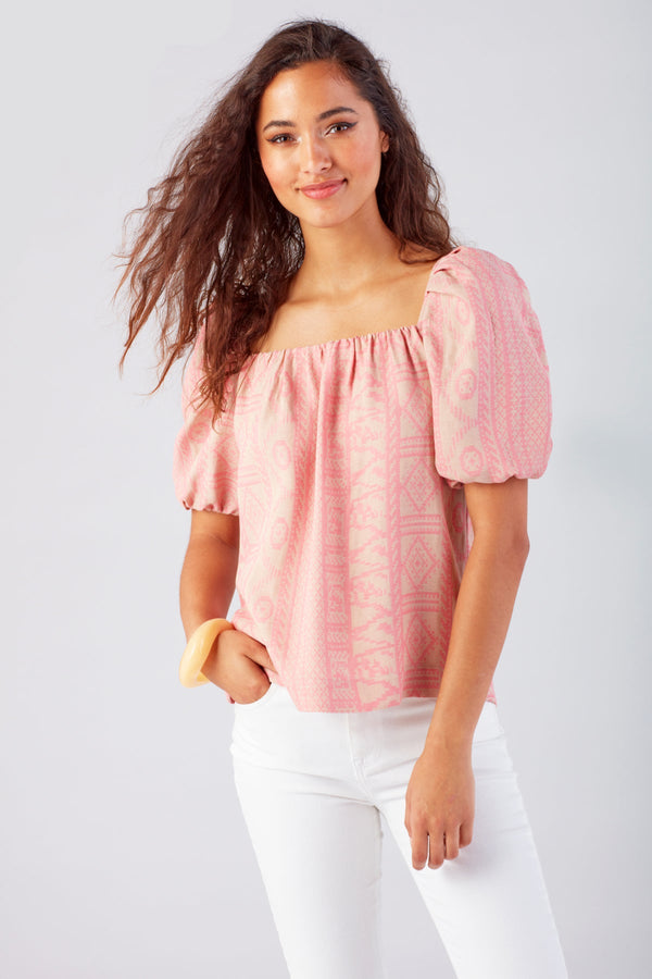 A model wearing the Finley bubble top, a casual short-sleeve jacquard blouse with a square neckline and a pink geometric pattern.