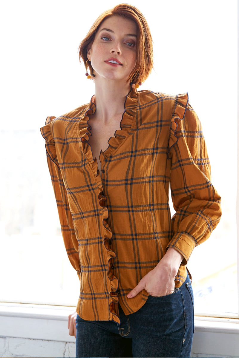 A model wearing the Finley Byrdee blouse, a long sleeve button down top with ruffle trim and an orange and black plaid print.