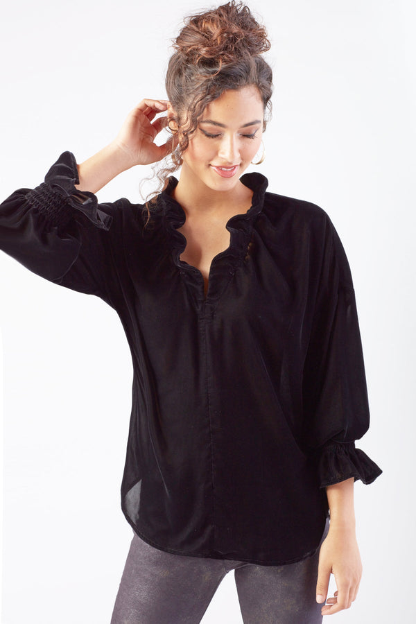 A model wearing the Finley Crosby blouse, a black whisperweight velvet top with a v-neck and ruffle detailing.