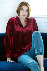A model wearing the Finley Crosby blouse, a burgundy red whisperweight velvet top with a v-neck and ruffle detailing.