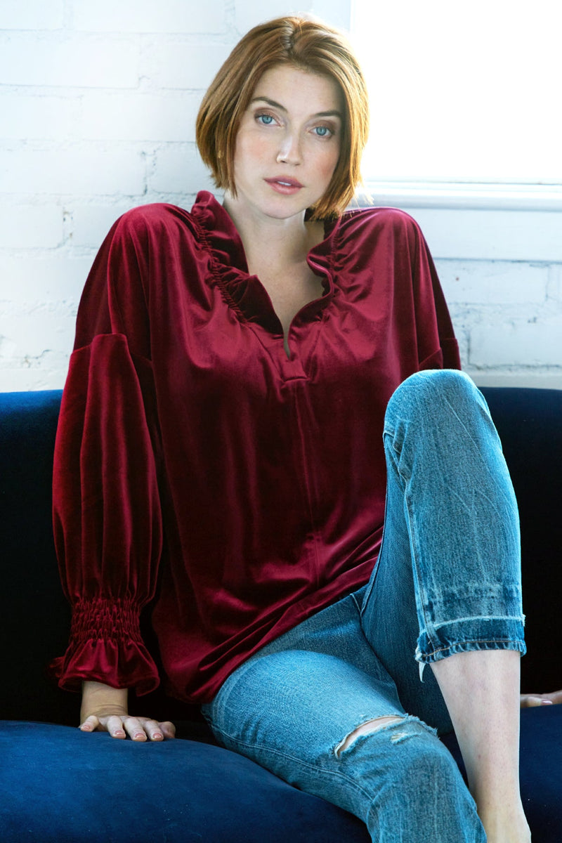 A model wearing the Finley Crosby blouse, a burgundy red whisperweight velvet top with a v-neck and ruffle detailing.