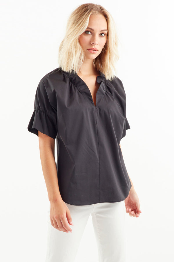 A blonde fashion model wearing the Finley Crosby shirt, a black poplin blouse with a ruffle collar and French sleeve detail.