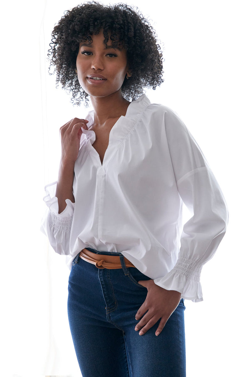 A Black model wearing the Finley Crosby blouse, a long sleeve white poplin button down top with ruffle collar and sleeve detail.