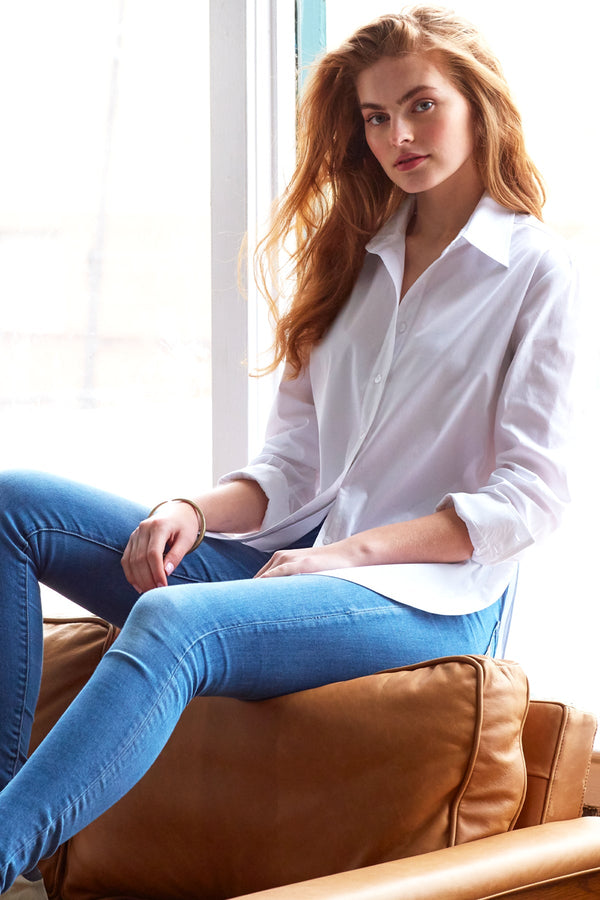 A model wearing the Finley Keller blouse, a casual white poplin button-down shirt with a high shirttail and a relaxed fit.