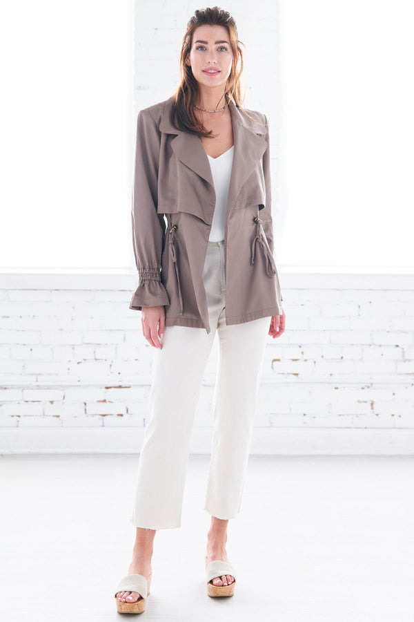 The Finley Sateen jacket, a double breasted drawstring jacket with a front tie, side seam pockets, and a pale brown color.